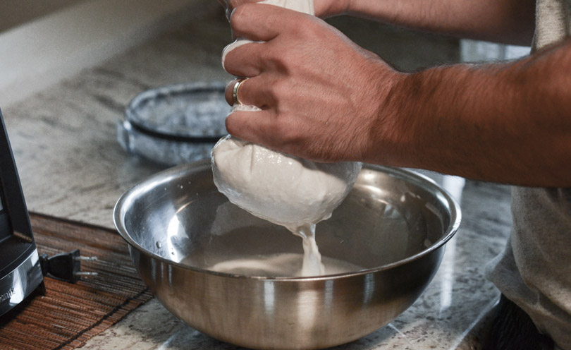 Squeezing almond milk through nut milk filtration bag.