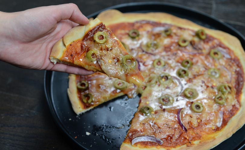 Pizza dough made in a Vitamix topped with vegan cheese, green olives, and onions.